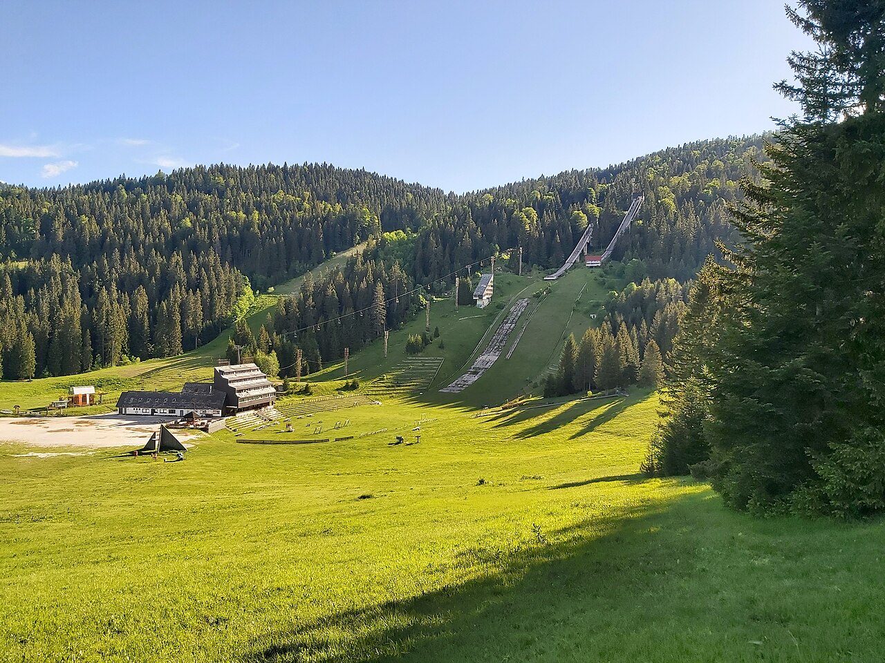 The Olympic ski jumps on Igman above a green meadow, with forest around them