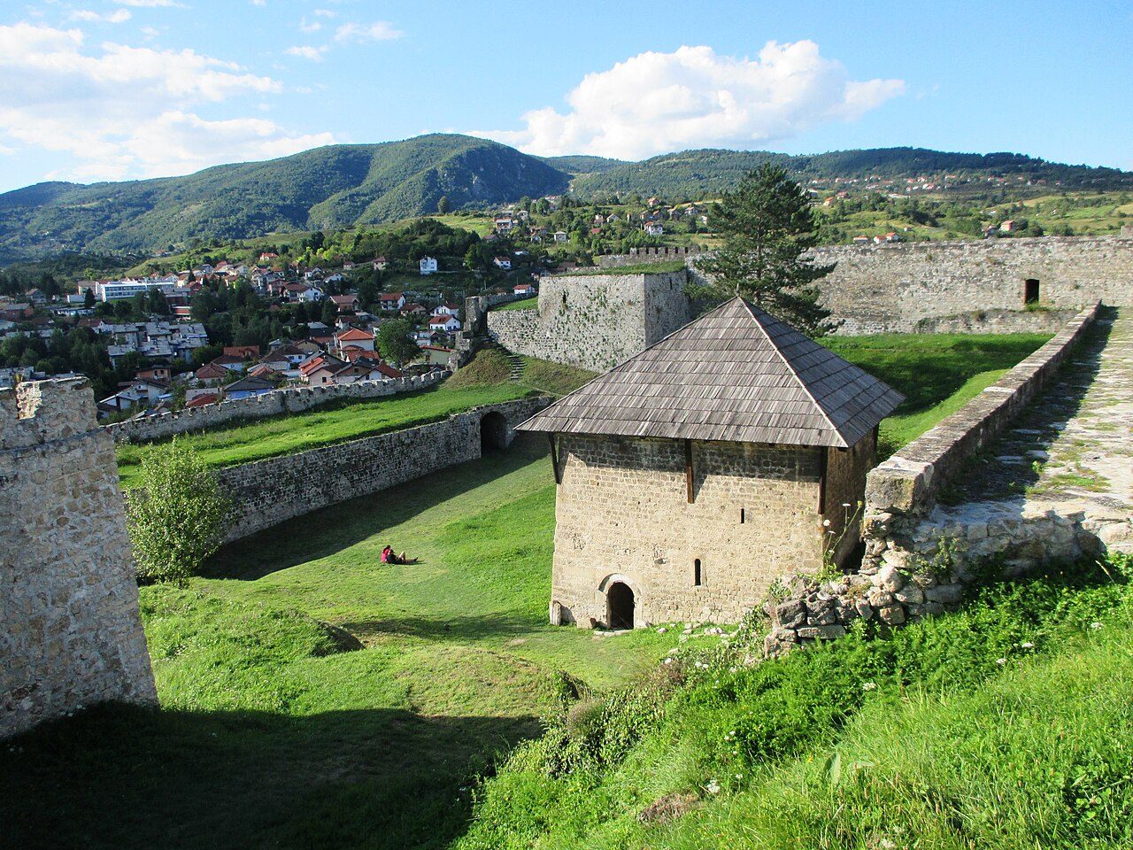 The grassy inner yard of Jajce Fortress, with its stone walls and the town below