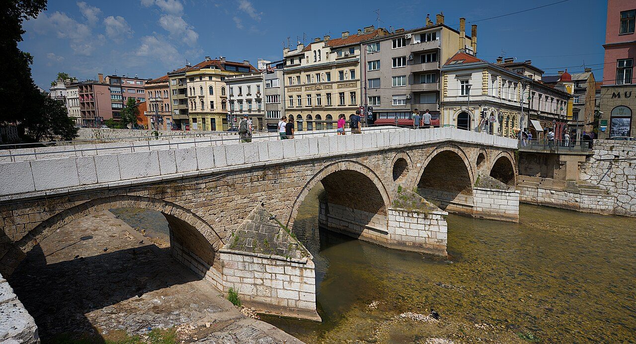 The stone arches of the Latin Bridge over the Miljacka, with Austro-Hungarian buildings behind