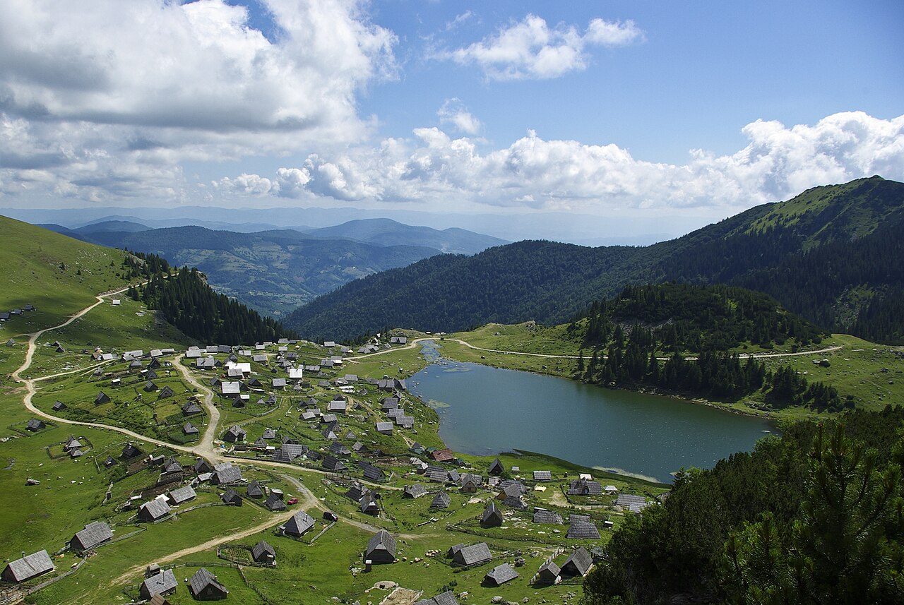 Prokoško Lake among green meadows and the wooden huts of the mountain village
