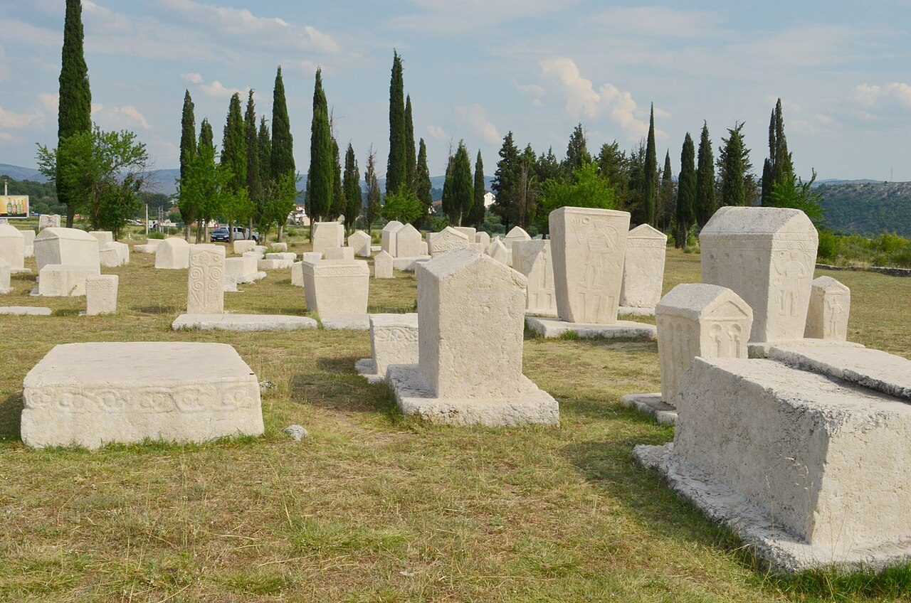 Rows of white stećci tombstones at Radimlja, with cypress trees behind