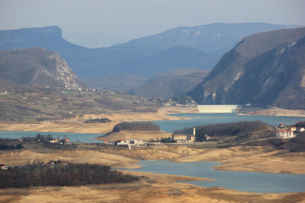 Rama Lake winding between hills and villages, with steep mountains behind