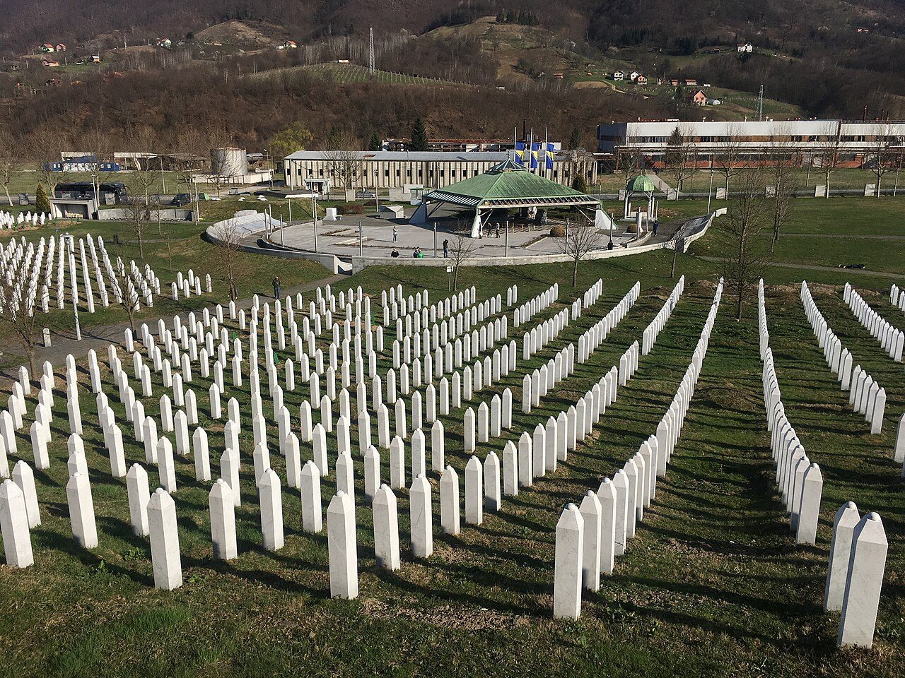 Rows of white gravestones at the Srebrenica-Potočari Memorial, with the memorial buildings behind
