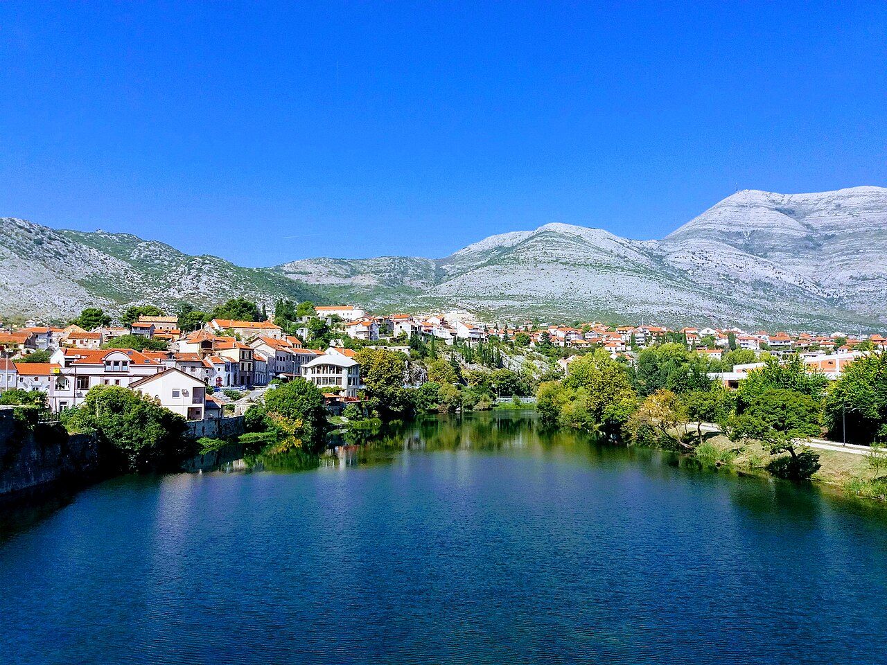 Trebinje's old town on the calm blue Trebišnjica river, with mountains behind