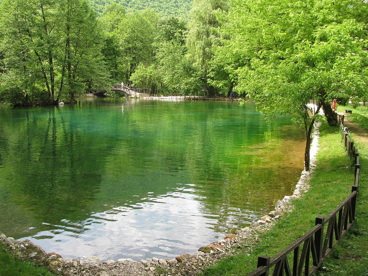 A clear green pool at Vrelo Bosne, framed by trees and a wooden fence